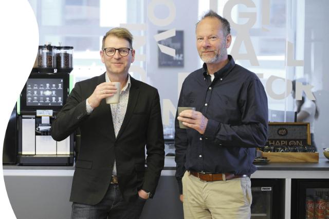 No Zebras CEO, Jesper Holm Joensen, og DanKafs konsulent, Lars Kier, står foran No Zebras kaffemaskiner med en kop kaffe i hånden